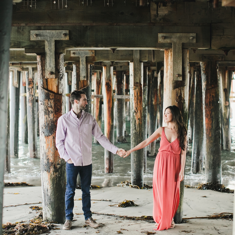 A couple holds hands under the pier at the boardwalk at sunset in Santa Cruz.