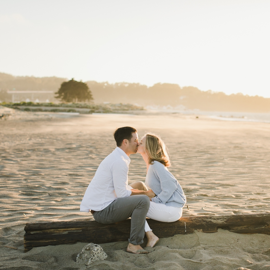 A couple kisses on a log at Crissy Beach in San Francisco during sunset.