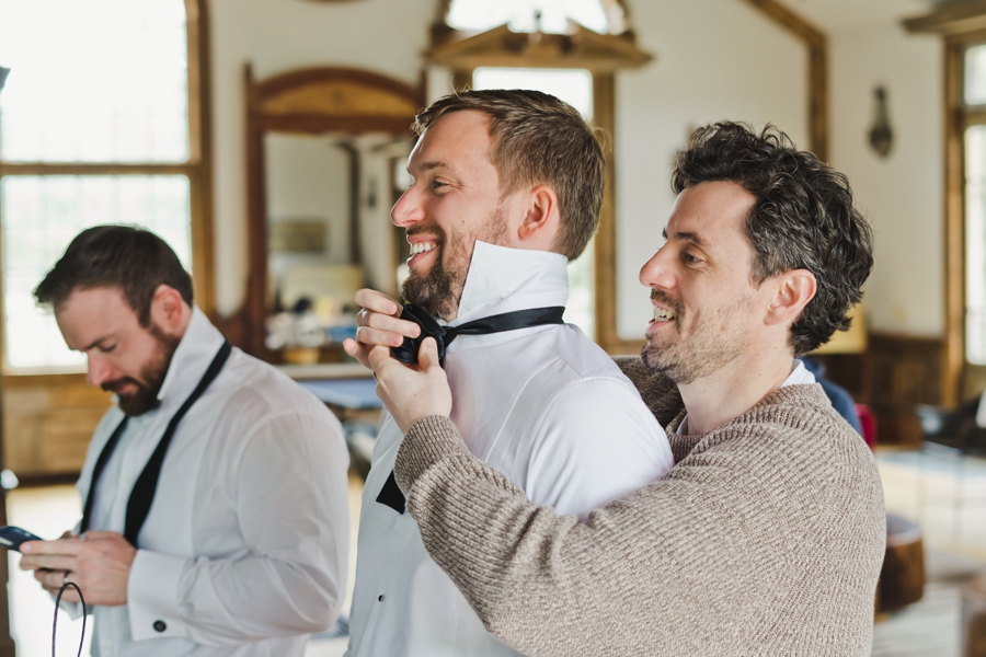 A groom has a friend help him put on his bow tie at Triple SSS Ranch in Calistoga, CA