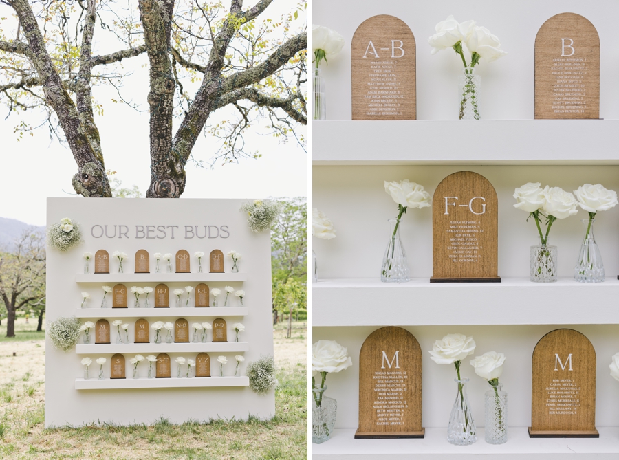 A white wooden wall of shelves with white flowers and name card assignments for a wedding reception