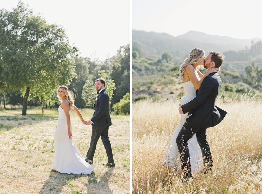 a bride and groom walk holding hands and kissing in a golden field.