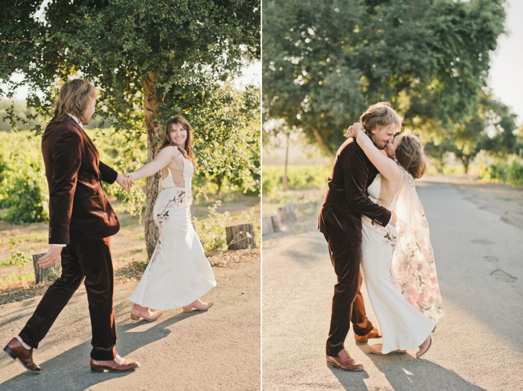 A couple in formal attire walks together and embraces on a sunlit outdoor path surrounded by greenery.